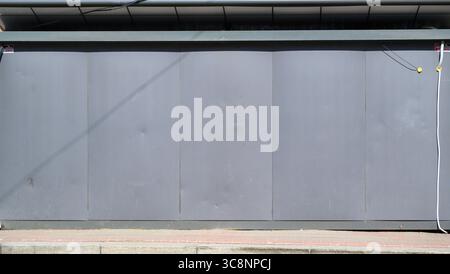 Les volets de vitrine en métal gris sont complètement fermés, protégeant une entreprise, avec des fils électriques suspendus sur le côté droit et un trottoir de briques à l'intérieur Banque D'Images