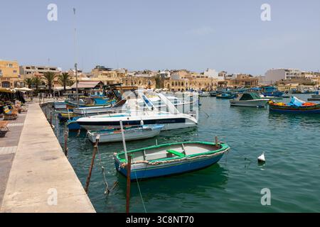 Marsaxlokk, Malte – 22 juin 2021 : bateaux de pêche colorés et yachts amarrés dans le port avec des bâtiments de la ville en arrière-plan. Banque D'Images