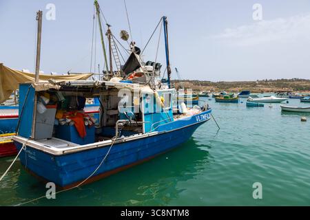 Marsaxlokk, Malte – 22 juin 2021 : bateau de pêche bleu amarré dans le port avec des bateaux traditionnels maltais en arrière-plan. Banque D'Images