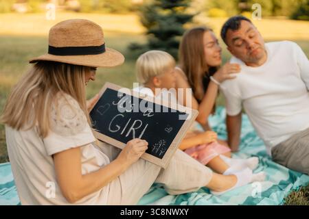 Famille célébrant une annonce de bébé avec pique-nique dans un parc ensoleillé Banque D'Images