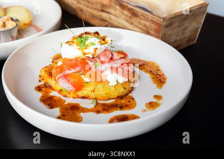 Une assiette de petit déjeuner gourmande avec saumon fumé, oeuf poché crémeux sur un rosti de pomme de terre dorée, garni de microgreens et accompagné d'une saveur Banque D'Images