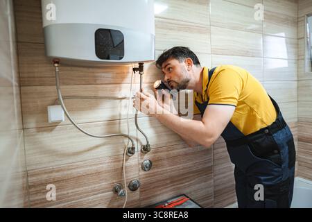 Plombier inspectant chauffe-eau avec lampe de poche dans la salle de bains Banque D'Images