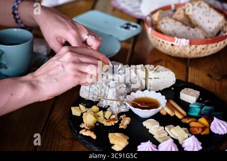 Les mains servent soigneusement le fromage à partir d'une planche de fromage magnifiquement arrangée avec différents types de fromage, noix et bonbons. Banque D'Images