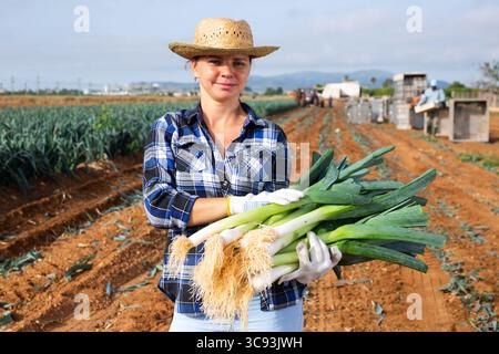 Horticulteur féminin réussi avec des poireaux dans les mains debout sur le terrain Banque D'Images