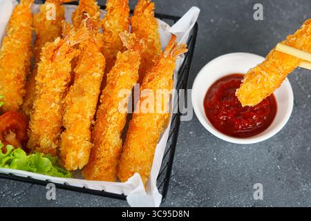 Crevettes frites brunes dorées, ou EBI Fry, trempées dans un petit bol de sauce à tremper par une paire de baguettes. Banque D'Images