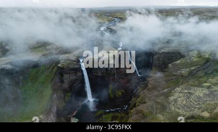 Deux superbes cascades plongent dans une vallée accidentée entourée de verdure luxuriants et de formations rocheuses spectaculaires en Islande. La brume se lève, créant une atmosphère mystique idéale pour l'aventure. Haifoss Islande Banque D'Images