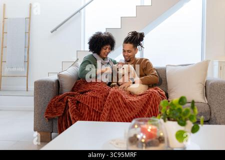 Couple afro-américain assis sur un canapé gris dans le salon caressant chiot jaune pâle avec lanterne Banque D'Images