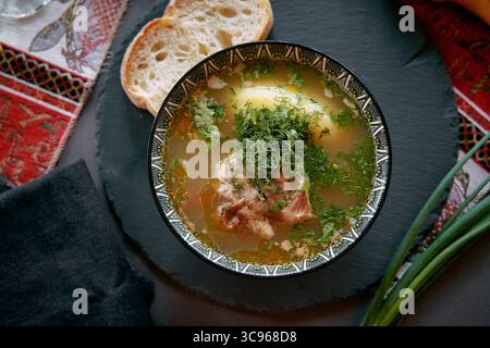 Un délicieux bol de soupe traditionnelle garni d'herbes fraîches, accompagné de tranches de pain sur une table rustique Banque D'Images