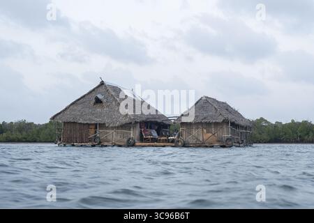 Vue d'une maison flottante avec toit de chaume et structure en bois se dresse sereinement sur l'eau dans un contexte de verdure luxuriante, Lamu, Kenya. Banque D'Images