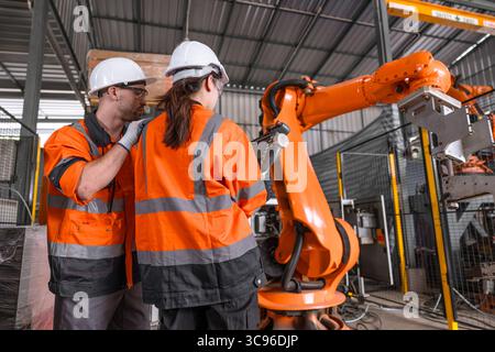 Ingénieur technicien robotique formation masculine aidant les jeunes femmes à contrôler l'équipe à opérer le bras de soudage robot dans l'usine moderne de l'industrie automatisée Banque D'Images