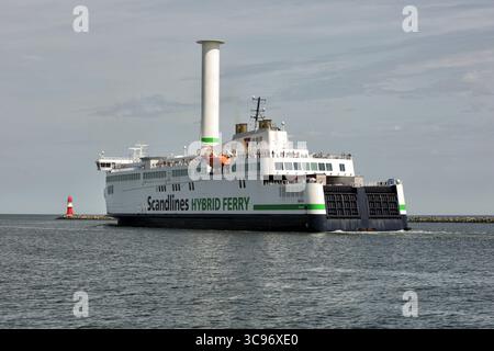 Mer Baltique, Allemagne - 11 juillet 2023 : vue d'un ferry hybride Scandlines naviguant sur les eaux calmes, son éolienne brille contre le ciel silencieux, avec un phare lointain marquant la côte. Banque D'Images