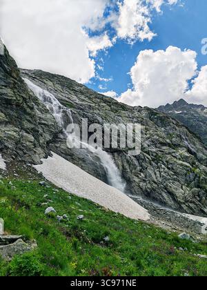 La superbe cascade coule sur un terrain rocheux entouré de verdure luxuriante et de fleurs sauvages vibrantes, créant une scène naturelle sereine Banque D'Images