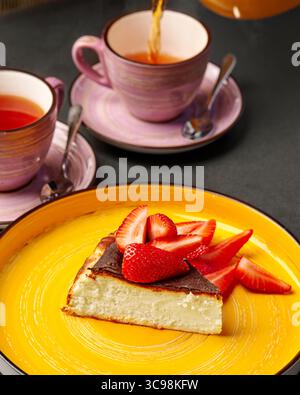 Délicieux cheesecake avec des fraises et deux tasses de thé versées Banque D'Images