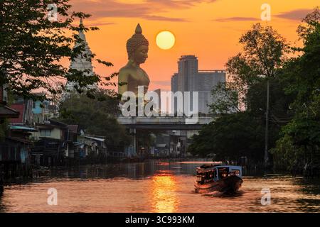 Un bateau passait devant la statue de Big Buddha (Phra Buddha Dhammakaya Thepmongkhon) dans le temple Wat Pak Nam Phasi Charoen situé près de la rivière pendant le coucher du soleil. Banque D'Images