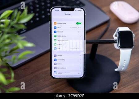 Poznan, Pologne - 29 juillet 2025 : un iPhone et une Apple Watch sur un socle de recharge de bureau, représentant ios 26 et Liquid Glass pour appareils numériques modernes Banque D'Images
