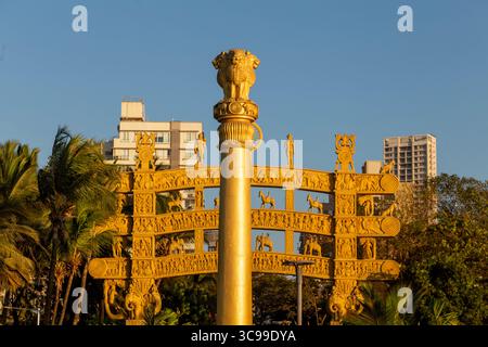Le pilier Ashoka doré et la passerelle ornée inspirée par Sanchi Stupa se dressent face à un ciel bleu clair, entouré de palmiers et d'une ville moderne Banque D'Images