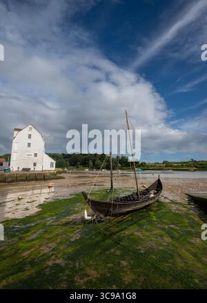 Vieux bateau en bois avec mât assis sur la boue. Vieux moulin à marée derrière. Vue sur le quai sur la rivière Deben dans la ville historique de Woodbridge dans le Suffolk, Royaume-Uni. Banque D'Images