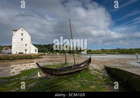 Vieux bateau en bois avec mât assis sur la boue. Vieux moulin à marée derrière. Vue sur le quai sur la rivière Deben dans la ville historique de Woodbridge dans le Suffolk, Royaume-Uni. Banque D'Images