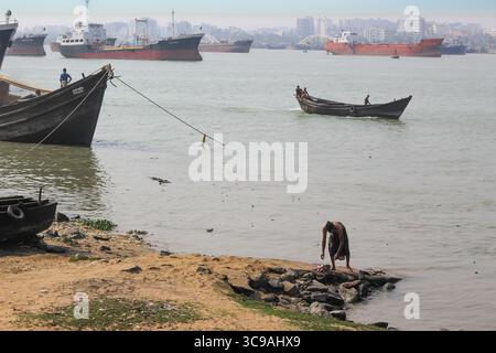 Chittagong, Bangladesh - 02 novembre 2018 : vue sur le port animé où les bateaux de pêche flottent aux côtés de cargos escarpés, un homme au bord du rivage, le tout sous un ciel brumeux. Banque D'Images