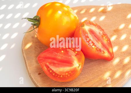 Nature morte des légumes - tomates rouges et jaunes sur une planche de bois sur fond blanc. Ombres abstraites, vue de dessus. concept d'été et vegetari Banque D'Images