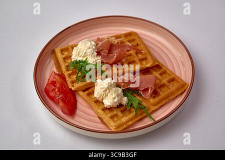 Gaufres délicieusement confectionnées garnies de crème, de prosciutto et de légumes frais servis sur une assiette décorative pour une expérience gastronomique Banque D'Images