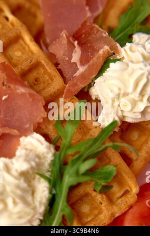Gaufres délicieusement confectionnées garnies d'une garniture fouettée crémeuse, de tranches de jambon frisées et d'Arugula fraîche, parfaites pour un délicieux petit déjeuner Banque D'Images