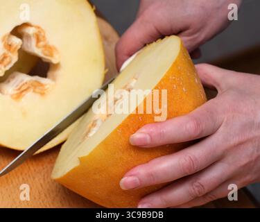 Les mains tranchent habilement une courge fraîche, révélant sa chair jaune éclatante à l'intérieur. Banque D'Images