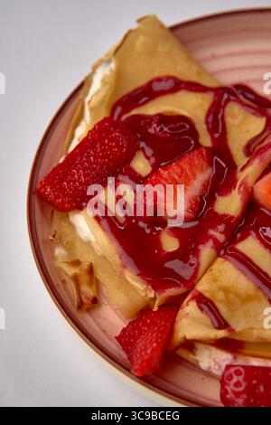 Délicieuses crêpes aux fraises avec garniture de sauce aux baies servies sur une assiette décorative, mettant en valeur une expérience de dessert sucré alléchante Banque D'Images