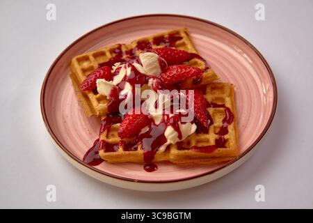 Gaufres délicieusement confectionnées garnies de fraises fraîches, d'une garniture fouettée crémeuse et d'un filet généreux de sirop sucré sur une assiette décorative Banque D'Images