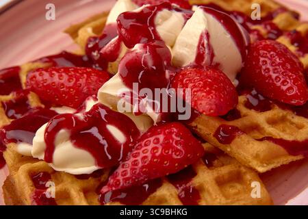 Gaufres délicieusement confectionnées garnies de crème glacée crémeuse à la vanille, de fraises fraîches et de sauce aux baies riches pour un délicieux dessert Banque D'Images