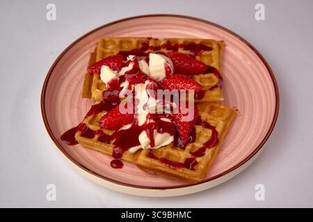 Gaufres délicieusement confectionnées garnies de fraises fraîches, de crème fouettée crémeuse et d'une sauce veloutée aux fraises pour un régal décadent Banque D'Images