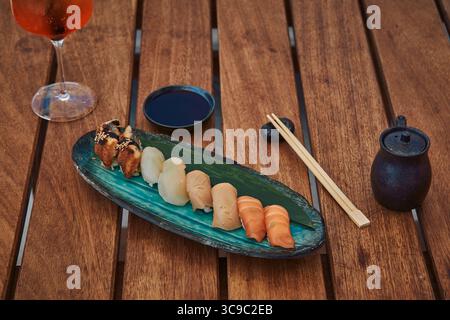 Une assiette exquise de sushis aux couleurs et textures variées magnifiquement disposées sur un plateau feuillu accompagné de sauce soja et de baguettes Banque D'Images