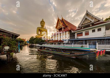 Un bateau passait devant la statue du Grand Bouddha (Phra Bouddha Dhammakaya Thepmongkhon ) dans le temple Wat Pak Nam Phasi Charoen situé près de la rivière au coucher du soleil. Banque D'Images