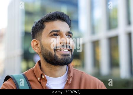 Un jeune Indien souriant regardant vers le haut réfléchi, encadré par une toile de fond urbaine floue. Banque D'Images
