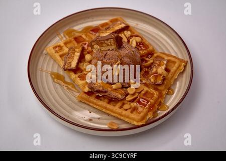Gaufres délicieusement délicieuses garnies de crème glacée au chocolat crémeuse, de cacahuètes croquantes et d'une sauce au caramel riche pour un délice sucré Banque D'Images