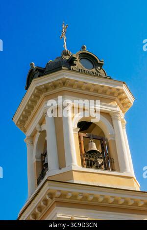 Une vue détaillée d'un clocher d'église historique avec des colonnes blanches, une inscription de 1881 et une croix dorée sur un ciel bleu vif. Banque D'Images