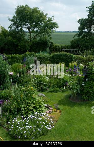 Un jardin animé rempli de fleurs et de plantes variées est entouré d'un paysage verdoyant sous un ciel partiellement nuageux. Banque D'Images