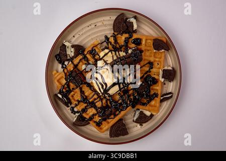 Gaufres délicieusement délicieuses garnies de crème glacée crémeuse, biscuits croquants et sauce au chocolat pour une expérience de dessert décadente Banque D'Images