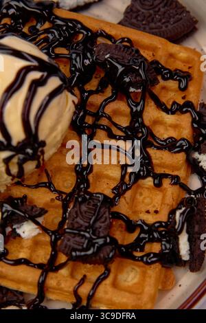 Gaufres délicieusement délicieuses garnies de crème glacée crémeuse, biscuits écrasés et sauce au chocolat pour une expérience décadente en dessert Banque D'Images