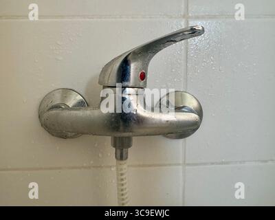 Gros plan d'une poignée de robinet de douche en métal montée sur un mur de salle de bain carrelé. Banque D'Images
