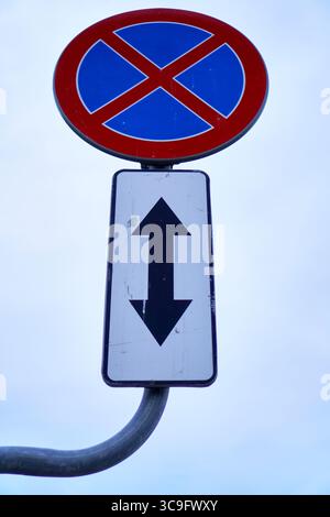 Panneau indiquant l'interdiction de stationnement sur le bord de la route et montrant une croix rouge et deux flèches verticales pour l'application des directives. Banque D'Images
