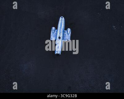 Vue aérienne d'une épave d'avion argentée, solitaire, reposant brutalement sur les sables volcaniques sombres de l'Islande. Banque D'Images