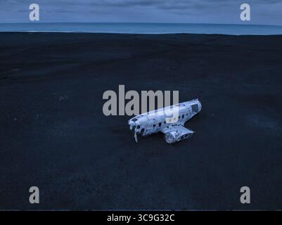 Vue aérienne d'une épave d'avion solitaire altérée reposant sur le sable noir et dur sous un ciel crépusculaire, Vik, Islande. Banque D'Images