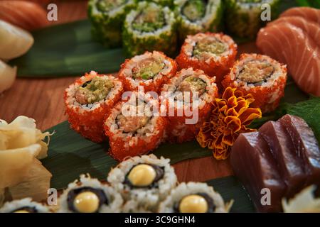 Un assortiment vibrant de Sushi Rolls avec des ingrédients colorés et des fruits de mer frais sur un plateau en bois avec des garnitures Banque D'Images