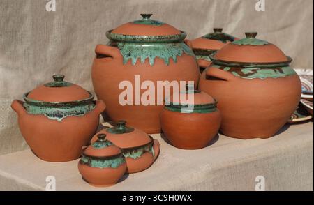 Une collection de pots traditionnels en argile de différentes tailles. Les pots ont un design rustique avec des accents verts et des couvercles. Ils sont disposés sur un backgrou neutre Banque D'Images