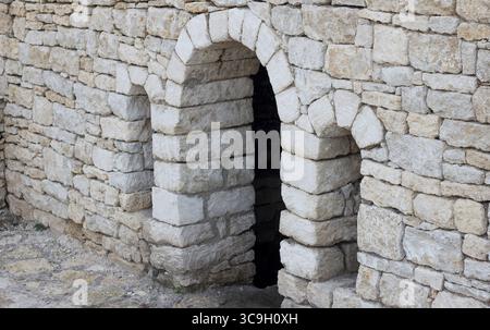Une ancienne arche en pierre faite de blocs grossièrement taillés. La structure montre des signes d'altération et d'âge, sur un fond neutre Banque D'Images