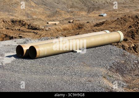 Deux grands tuyaux en fibre de verre beige reposent sur du gravier dans une zone de terrassement active, illustrant l'échelle et la préparation pour l'utilité souterraine Banque D'Images