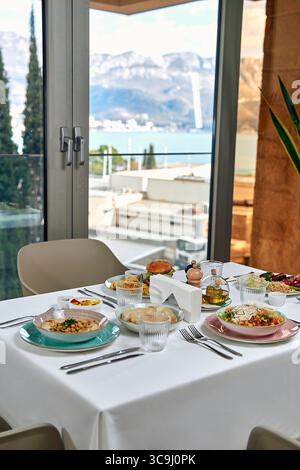 Une table de petit déjeuner somptueuse avec des plats variés sur une vue panoramique sur les montagnes et l'eau dans une salle à manger moderne Banque D'Images