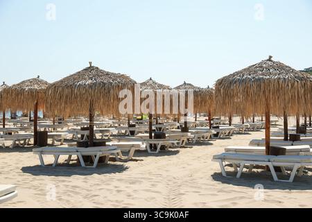 Superbes parasols en paille et transats sur une plage de sable Banque D'Images