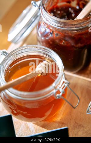 Un gros plan sur le miel naturel délicieux et la confiture riche en pots rehaussés avec des plongeurs en bois et des couleurs invitantes sur une surface en bois rustique Banque D'Images